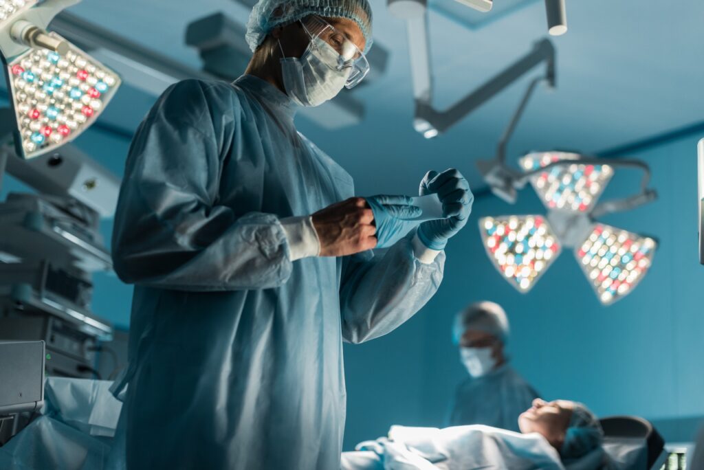 surgeon taking off medical gloves near patient in surgery room